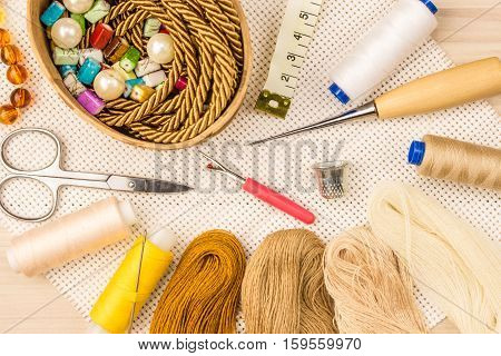 Scissors buttons thread measuring tape and sewing supplies on the cloth and light wooden background. The view from the top.