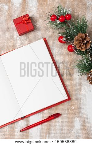 Christmas composition with red notebook small red gift box red pen and spruce branch with red berries and cones. Concept christmas new year plan. Flat lay vertical orientation.