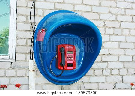Red payphone in the blue booth on a white brick wall.