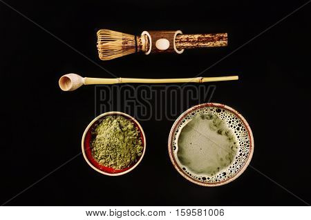 Chasen - special bamboo whisk, spoon for matcha tea and beverage with apetite foam. Black background. Photo made in flat lay style. Focus is on matcha foam.