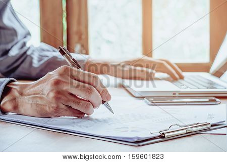 Business man hand working with laptop computer and writing business graph or analysis chart on modern desk table. close up. Business concept
