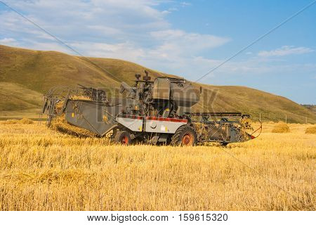 Harvester removes the ripened wheat crop on the field on the backdrop of picturesque mountains