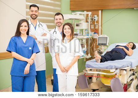 Portrait of a group of four doctors and nurses standing in a hospital room with a patient and smiling