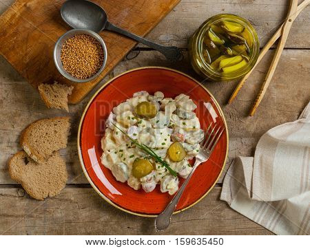 Homemade German potato salad with frankfurt sausages on a rustic table with bread pickles and mustard seeds.