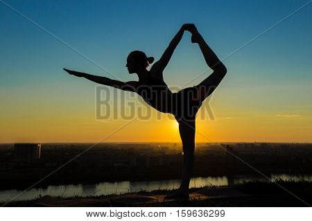 Silhouette of sporty woman practicing yoga in the park at sunset - lord of the dance pose. Sunset light. Freedom, health and yoga concept