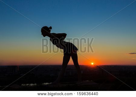 Silhouette of sporty woman practicing yoga in the park at sunset. Sunset light, golden hour. Freedom, health and yoga concept