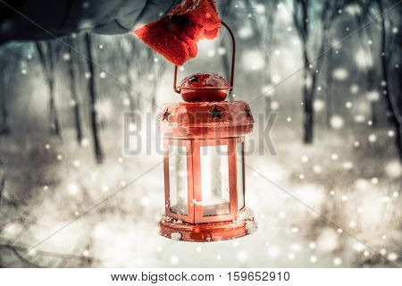 Holding in red glove a red candle lantern in the winter forest. Snow forest snowfall. Christmas Winter New Year background trembling flame Scenery. Fairy magic forest flashlight