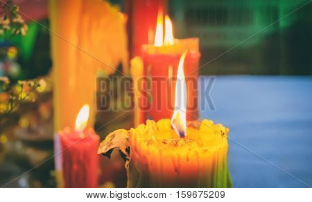 Burning red and yellow beautiful old textured candles with defocussed background of buddhist temple Thailand. Mood of sacrament and revelation.