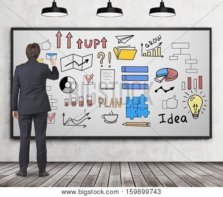 Rear view of a businessman in a suit who is drawing a colorful startup idea sketch on a whiteboard hanging on a conrete wall