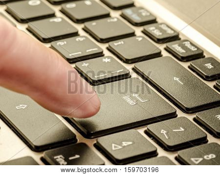 close up of a personal computer with italian keyboard with enter command and a finger that is going to press it