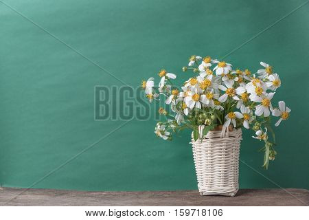 white flowers in basket on wooden table with old green background vintage tone.