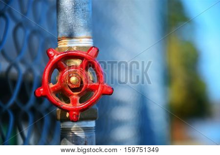 A selective focus image of a red shut off valve against a chain link fence.