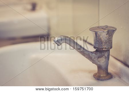 Old faucent in the restroom. Wasting water water tap in dirty public toilet.