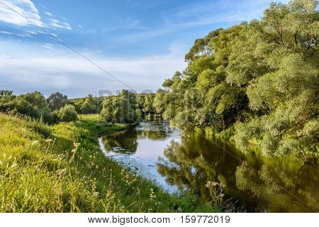 Summer warm evening. River view from the shore. Reflection of blue sky in the river water.