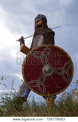 Knight on a rock with a sword against blue cloudy sky