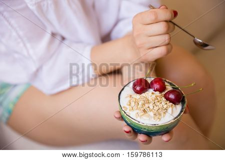 Closeup of woman's hands holding a cup with organic yogurt with oats and cherries. Homemade vanilla yogurt in girl's hands. Breakfast or snack. Healthy eating and lifestyle concept.