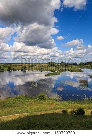 Clouds above the river, overgrown with water lilies, the sky reflected in the water