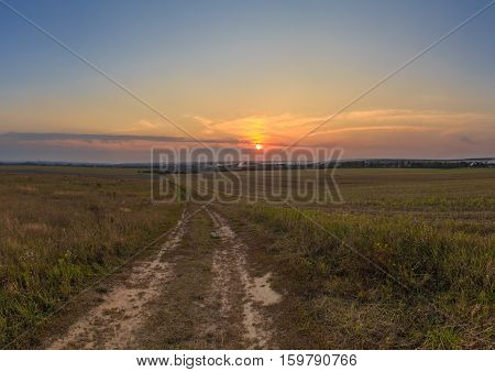 The road through the field with a hill at sunset, horizontal frame