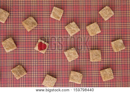 Sugar cubes with a red heart on one of them as background. Top view. Diet unhealty sweet addiction concept