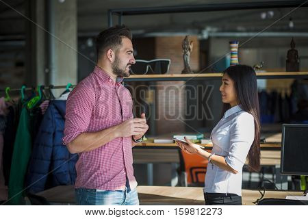Happy businessman and businesswoman standsing face to face and discussing certaing business projects or strategies while working in office interior. Freelance concept.
