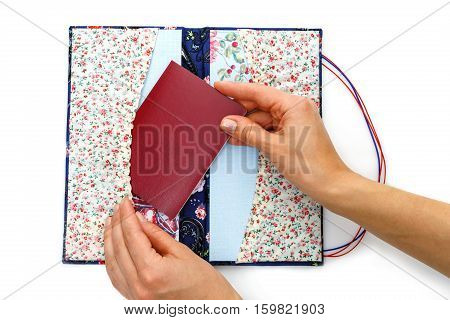 Beautiful handmade scrapbooking holder for travel documents with ribbon closure. Floral fabric design. Femae hands putting passport in. isolated on white background.