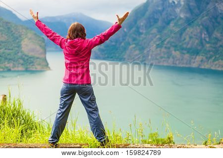 Travel concept. Happy free tourist woman in happiness and elated enjoyment with arms raised outstretched up looking at fjords mountains in Norway