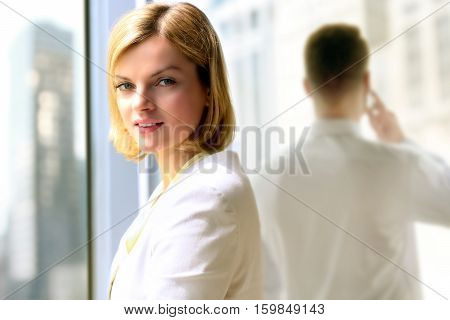 Portraits of business woman standing near window. Man talking on a mobile phone