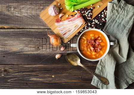 Homemade bean soup in white bowl on rustic wooden background with ingredients. Top view.
