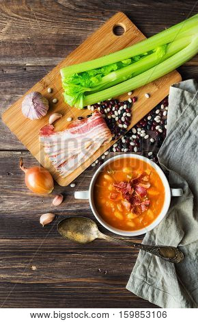 Homemade bean soup in white bowl on rustic wooden background with ingredients. Top view.