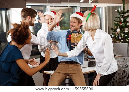 Happy cheerful colleagues celebrating christmas party in office smiling giving presents.
