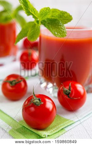 Tomato juice in a glass with a cherry and mint on a light background