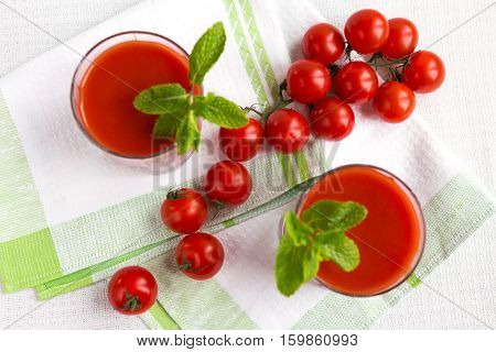 Tomato juice in a glass with a cherry and mint on a light background