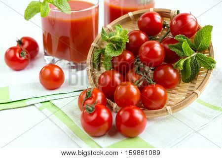 Tomato juice in a glass with a cherry and mint on a light background