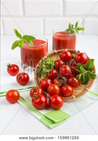 Tomato juice in a glass with a cherry and mint on a light background