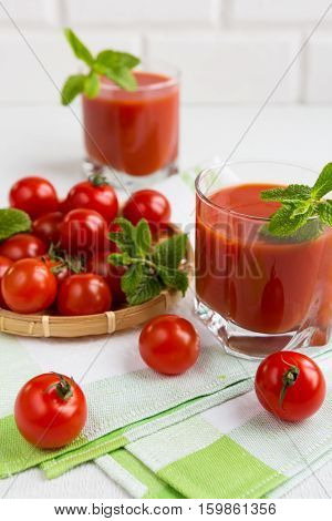 Tomato juice in a glass with a cherry and mint on a light background