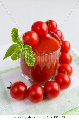 Tomato juice in a glass with a cherry and mint on a light background