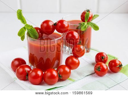Tomato juice in a glass with a cherry and mint on a light background