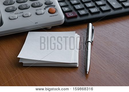telephone calculator white paper for notes and metal ballpoint pen lying on a light wooden table in the office at work preparing for the working day and making cold calls to clients