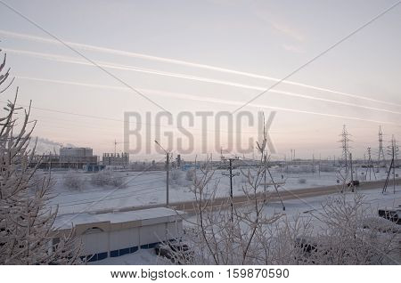 Pink sunset on the winter industrial street with prints in the sky after the airplane  View from window in the cold frosty evening. Road with cars