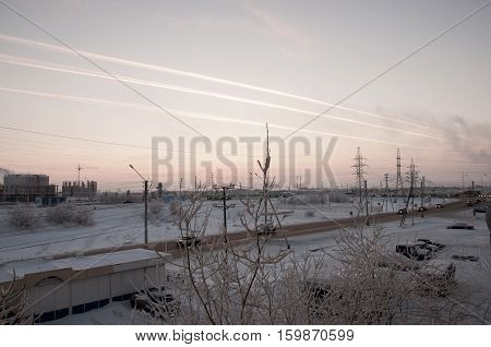 Pink sunset on the winter industrial street with prints in the sky after the airplane  View from window in the cold frosty evening. Road with cars