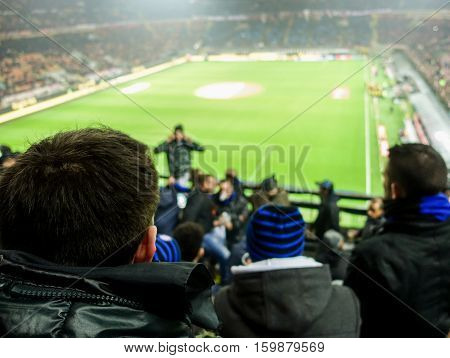 Soccer fans celebrate their team in football italian stadium - People watching sport match singing and screaming - Love for sport concept - Soft focus on man head jacket - Warm filter