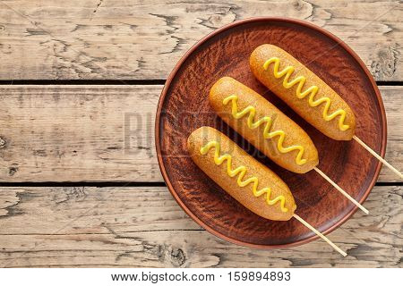 Corn dog traditional American junk food fried hotdog meat sausage snack with mustard snack treat coated in a thick layer of cornmeal batter on stick unhealthy eating on rustic wooden table.