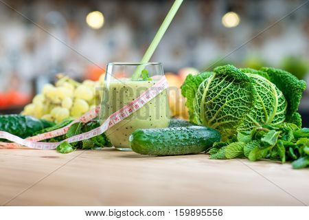 Glass with smoothie with green vegetables on the table in the kitchen. Healthy vegetarian diet for weight loss and detox
