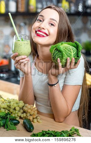 Portrait of young smiling woman with green smoothie in the kitchen at home. Healthy vegetarian diet for weight loss and detox