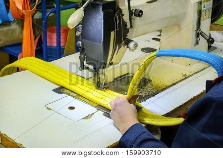 Industrial sewing machine sews a webbing sling. Manufacture of textile slings and tie straps.