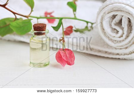 Essential oil glass bottle extract, delicate pink tropical flower, white towel. Botanical beauty and health care.