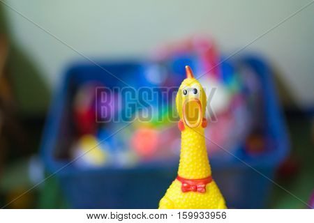 Toy rubber shriek yellow chicken on blur toy background in messy room kid room shellow DOF