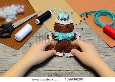 Child holding a cute gingerbread man ornament in his hands. Christmas tree gingerbread man ornament, handicrafts supplies on old wooden table. Christmas felt diy for kids. Homemade sewing concept