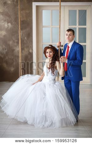 Wedding. Happy young bride sitting on swing and groom. Marriage concept