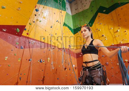 Do it better. Pretty delighted young woman using climbing equipment while standing in climbing gym and enjoying her hobby.